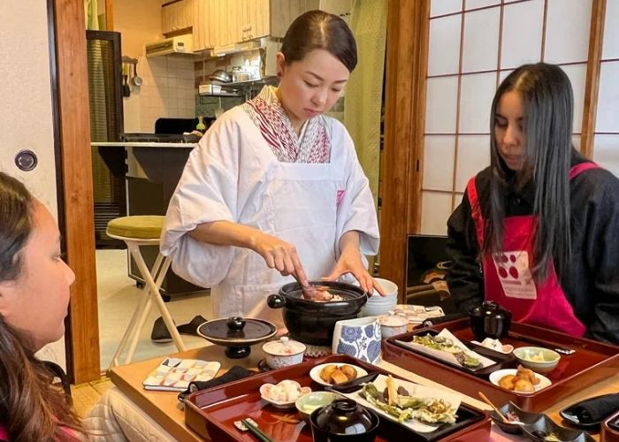 A host is mixing ingredients at a vegan cooking class in Tokyo while two guests watch.